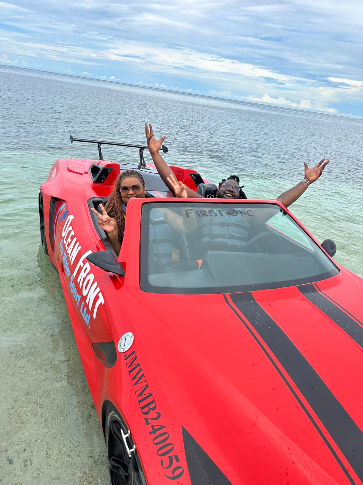 Two smiling guests waving from a red water car in the sea