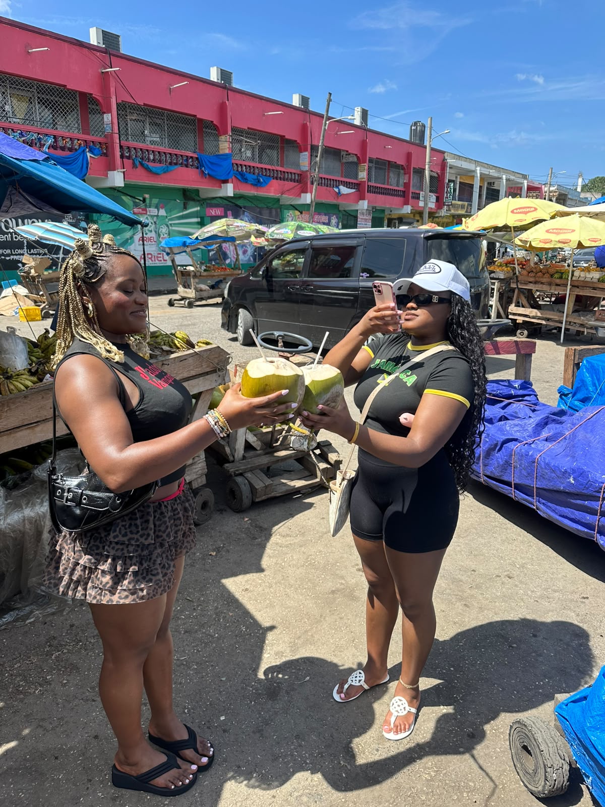 Two guests enjoying fresh coconuts at a colourful Jamaican market